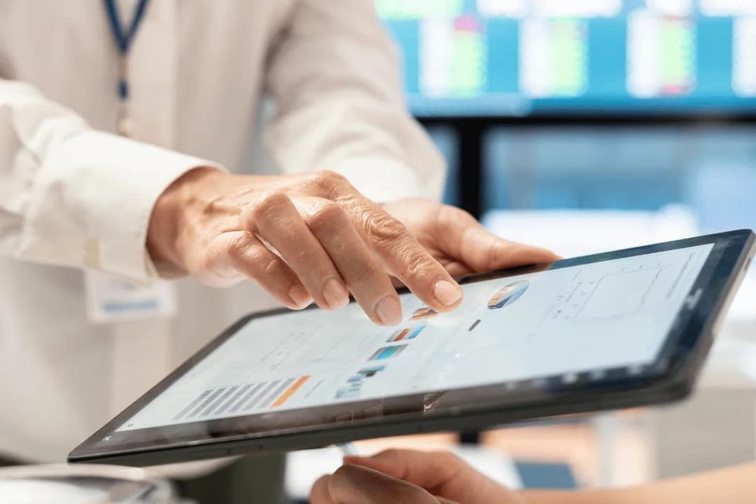 Hands interacting with a tablet displaying charts and graphs in an office setting, conveying a sense of collaboration and data analysis.